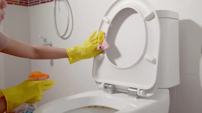 亚洲妇女用液体喷雾和粉色布擦拭厕所的手清洁马桶座圈