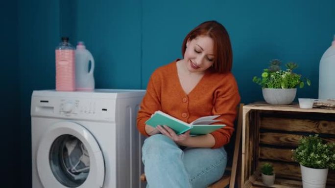 年轻的红发女人在洗衣房等着洗衣机看书