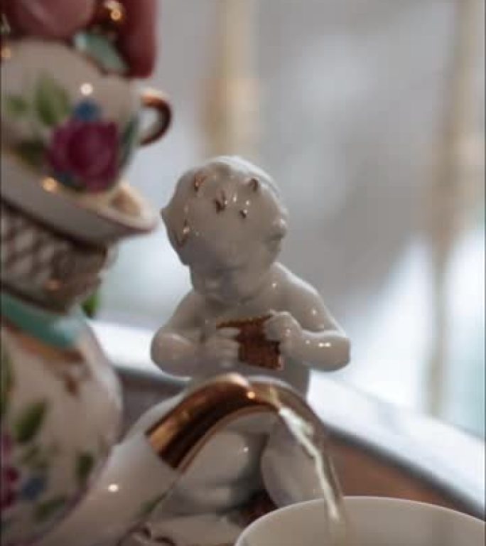 白瓷天使小雕像和手倒茶从华丽的茶壶到茶杯