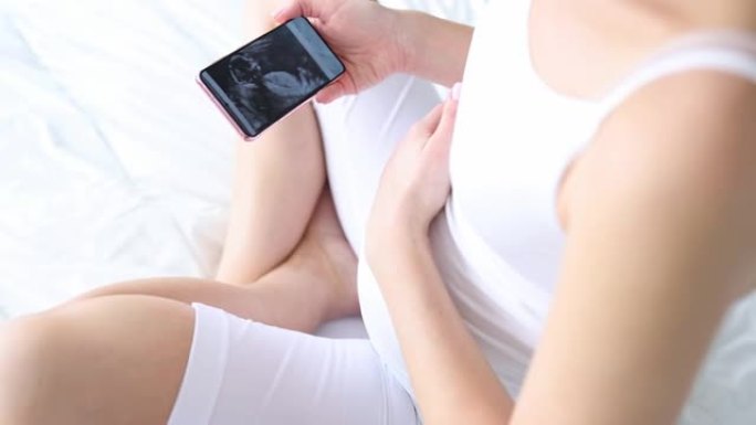 孕妇坐在床上看手机超音波图片特写4k电影慢镜头