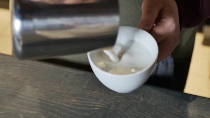 咖啡师将泡沫牛奶倒入卡布奇诺杯中。特写，慢动作