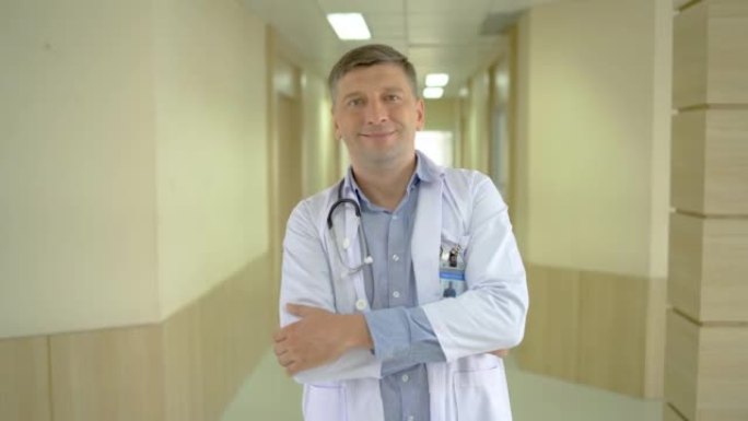 微笑快乐快乐的男性医生医务人员的肖像穿着白色长袍，脖子上戴着听诊器站在现代医院诊所，双臂交叉看着相机