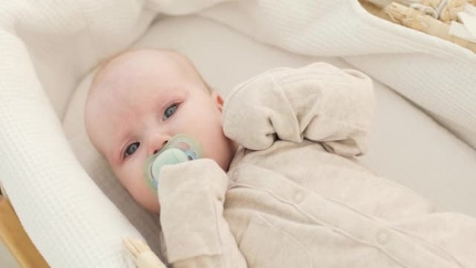 一个可爱的婴儿，嘴里叼着奶嘴，躺在白色毯子上，穿着白色衣服，抽泣着