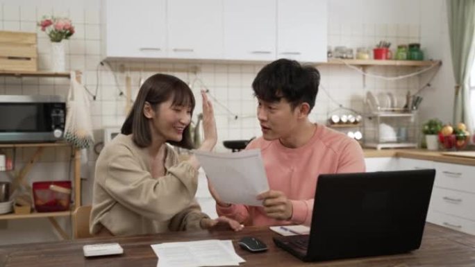 兴奋的亚洲配偶们在家里的餐厅里读着写有好消息的信。他们为获得退税而击掌庆祝