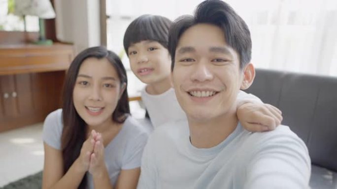 亚洲家庭可爱的儿子，爸爸和妈妈坐在沙发上对亲戚表示敬意，在智能手机视频通话时，他们在家里的客厅里一起