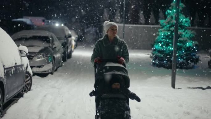 下雪时，年轻的母亲推着婴儿推车在城市街道上行走。白雪覆盖的树木和灌木丛。在美丽的冬夜陪宝宝。享受宁静