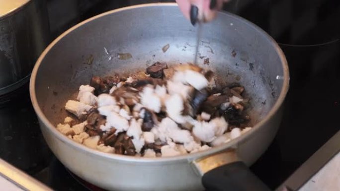 一位年轻女子的手在热锅中加入切碎的肉到炸蘑菇中