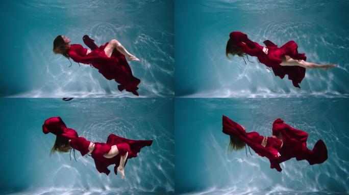 一个年轻女子在水下游泳的神奇水下镜头。红色连衣裙