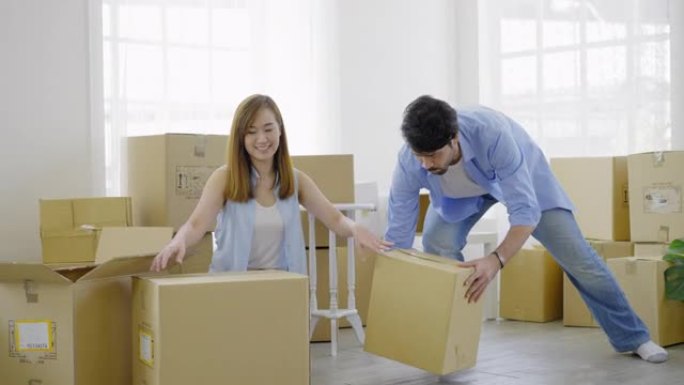 幸福的年轻夫妇打包纸箱，准备搬到新家或公寓。美丽的年轻女子打包纸箱，开心地微笑着，而她的丈夫拿着纸箱