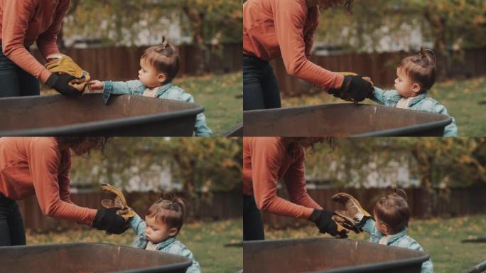 蹒跚学步的女孩帮助妈妈在后院捡树叶