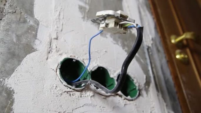电开关挂在混凝土墙上的插座盒上的电线上。电的危险