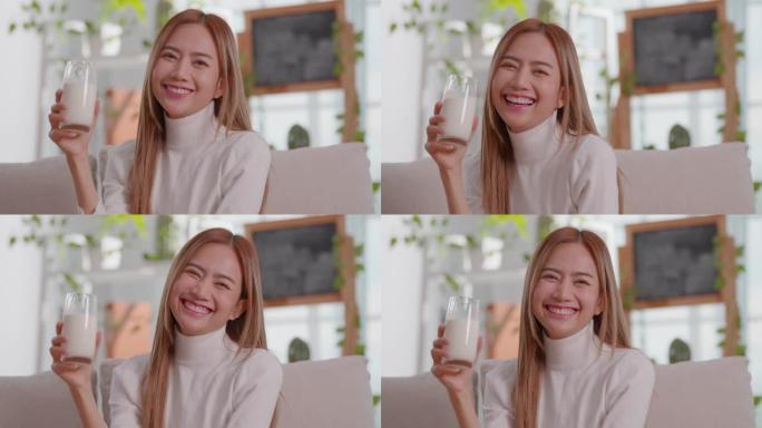 健康的年轻亚洲妇女喝牛奶与钙的强壮的骨骼看着相机。微笑的女人在玻璃杯上拿着豆浆享受营养健康生活，天然