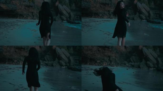 下午穿着黑色连衣裙在沙滩上奔跑并摔倒的女人