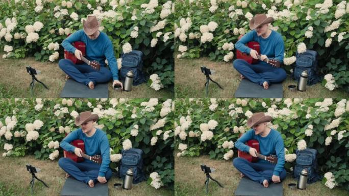 带着吉他的Man traveler坐在大自然的公园里进行在线广播