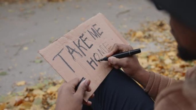 年轻的黑人搭便车在路上在纸板上写字