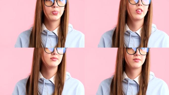 剪辑视频，一个漂亮的年轻金发少年戴着眼镜，在粉红色背景下摆出口香糖泡泡。