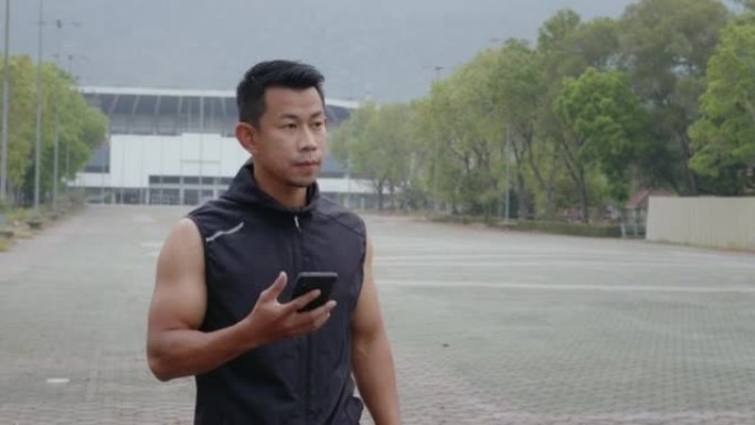 亚洲年轻人在体育俱乐部体育场户外慢跑，并在智能手机上观看设备屏幕。