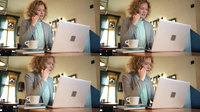 忙碌的女商人在现代餐厅使用笔记本电脑时在手机上聊天