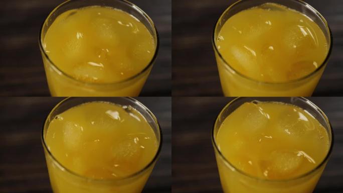 冰块的俯视图旋转并漂浮在木制桌子上的高玻璃杯中的新鲜橙汁中