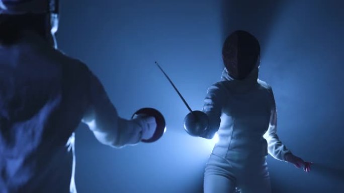 从后面看两名运动员击剑运动员参加比赛。戴着击剑面具的女人互相攻击，用重剑攻击。黑暗工作室，背光蓝光和