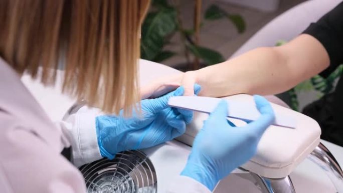 美容院美甲专家清洁角质层专业指甲锉在美容院美甲时戴着蓝色防护手套。