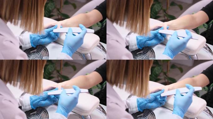 美容院美甲专家清洁角质层专业指甲锉在美容院美甲时戴着蓝色防护手套。