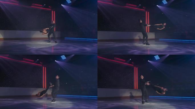 花样滑冰运动员对在聚光灯下进行固定旋转提升。男人抱着女人的两个脚踝，双臂交叉，旋转，她盘旋在冰上，双
