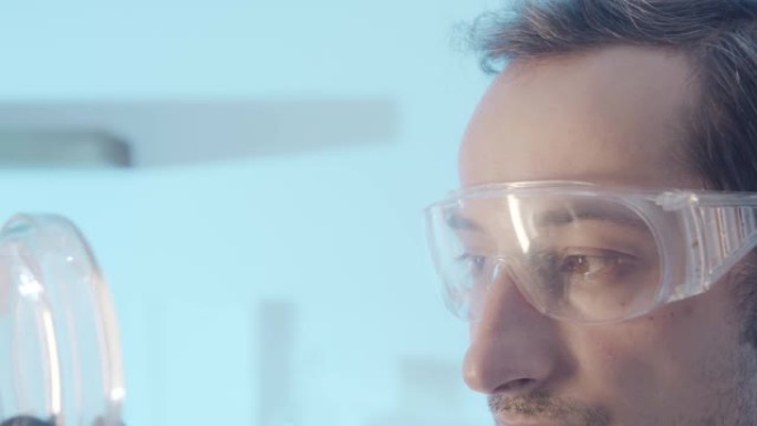 特写肖像。戴着保护性实验室眼镜的棕色眼睛男人的脸的一部分。医生专注于检查培养皿中的物体。