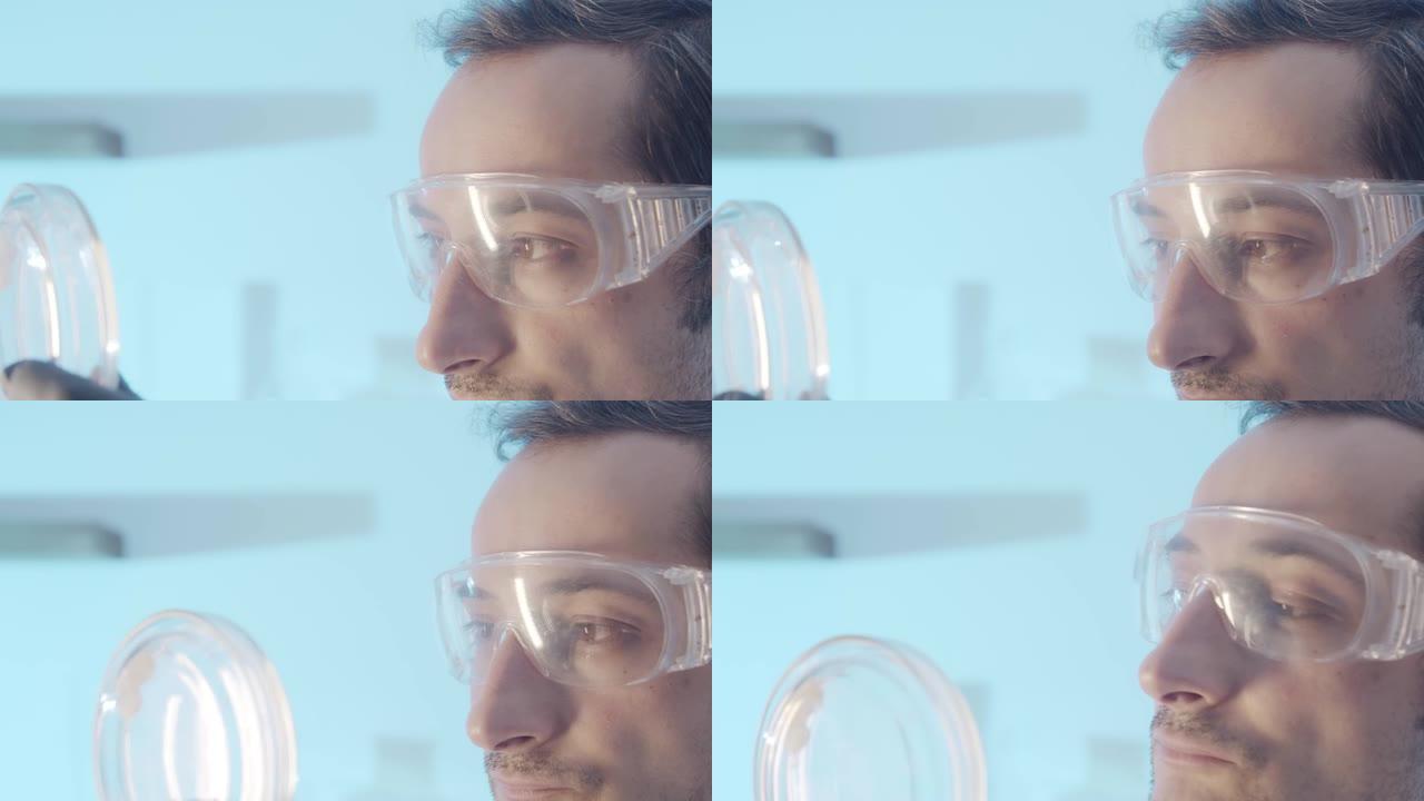 特写肖像。戴着保护性实验室眼镜的棕色眼睛男人的脸的一部分。医生专注于检查培养皿中的物体。