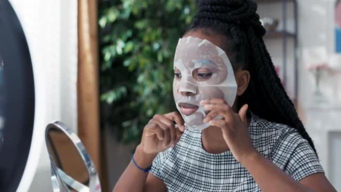 Influencer records美容教程将面膜应用于面部使用手机的环形灯，博客作者谈论皮肤护理用