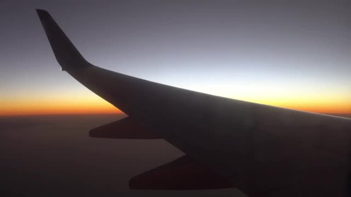 日出时飞机的机翼挡住了阳光。从飞机的窗户看。飞机在日落时飞行。乘飞机旅行。