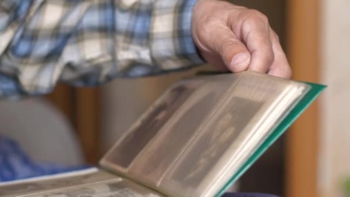 一位老人的手翻阅一本旧的家庭相册的特写。选择性聚焦，浅景深。养老金领取者对青年的记忆激增。