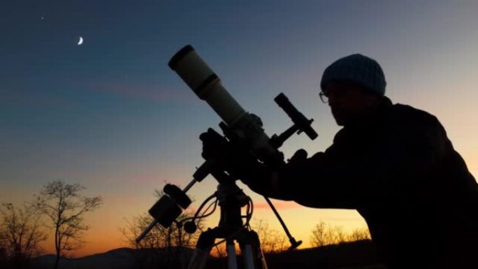 夜空下男人、望远镜和乡村的轮廓。