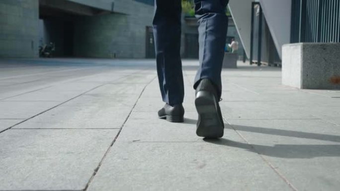 商人上班的后视脚。穿着皮鞋和正装的自信的企业家在办公楼附近走在市中心的后景。