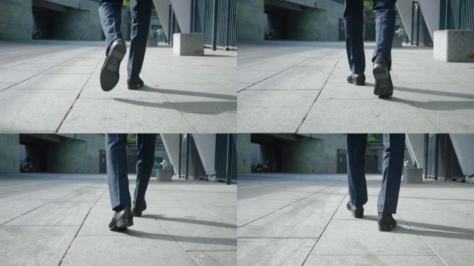 商人上班的后视脚。穿着皮鞋和正装的自信的企业家在办公楼附近走在市中心的后景。
