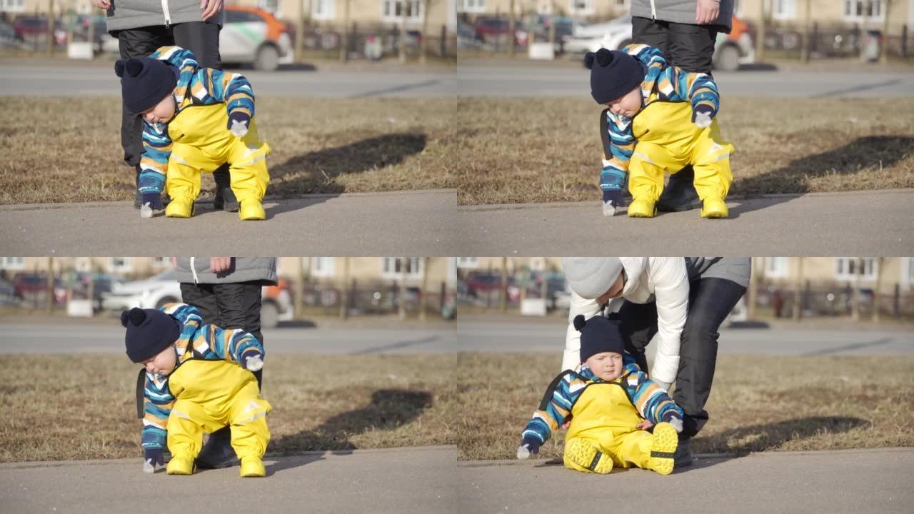 妈妈带着可爱的小孩穿着黄色防水雨裤围兜，供孩子们在人行道上行走，一岁的男婴在寒冷的季节学习走路。