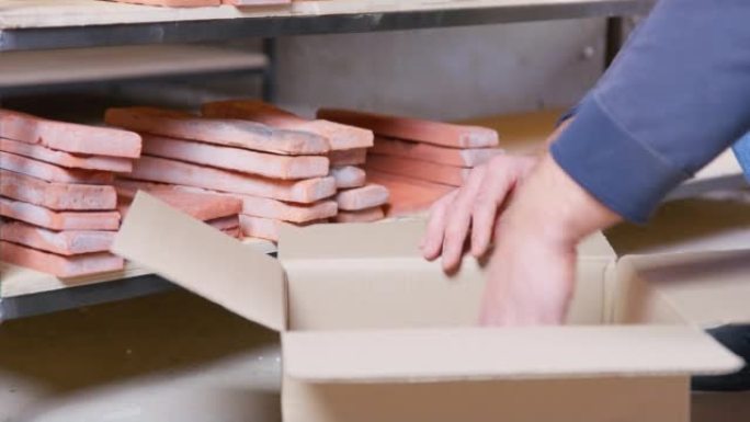 熟练的工人将手工制作的陶土砖从木架子上放入纸盒中。车间特写制作瓷砖的装饰块