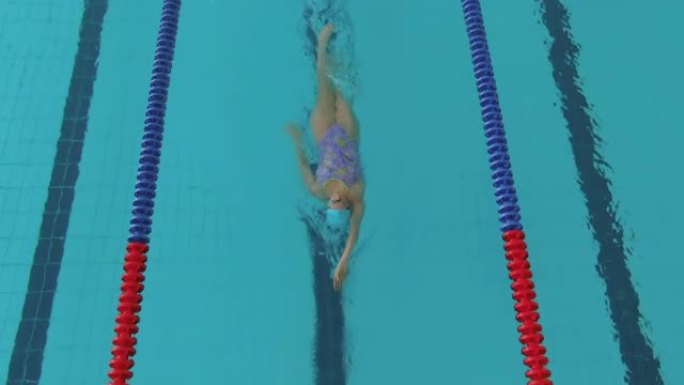 年轻女子在体育游泳池里爬着做运动。戴着护目镜和泳衣的女人在她的背上游泳，用手划船。大型运动游泳池，有