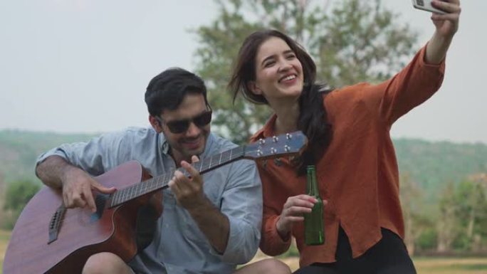 浪漫情侣旅行者在野营中弹吉他和唱歌时自拍。