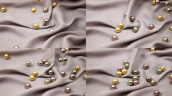 珍珠珠子不同颜色在灰色丝绸上滚动，背景，慢动作