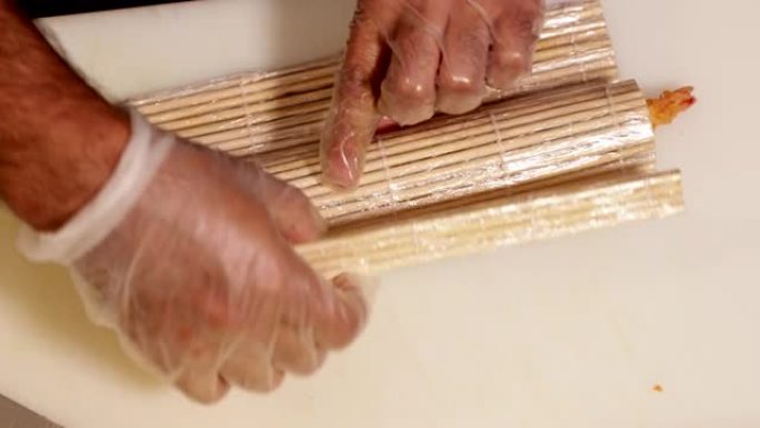 厨师使用竹垫将鳄梨片放在带有虾天妇罗馅的寿司饭上