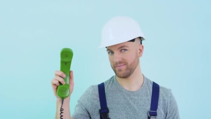 一个穿着工作服、戴着头盔的修理工手里拿着一个旧手机，指着它