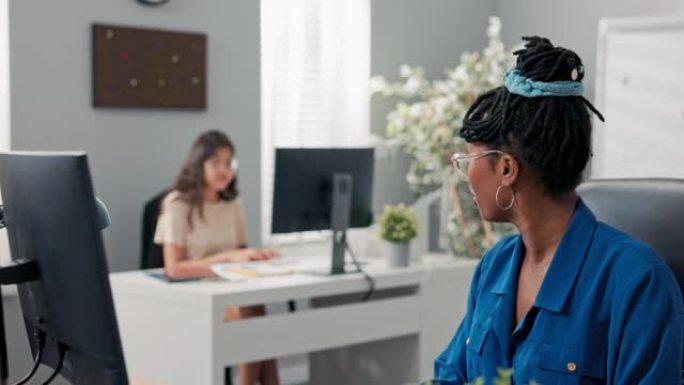 在办公室忙碌的下午，两个优雅的女人在公司的电脑前工作，在键盘上单击手指，彼此交谈，开玩笑，关心协作关
