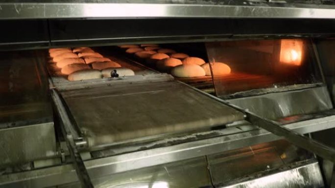 面包师手动拉动甲板烤箱装载机，将生面包面团移入烤箱-在面包店制作面包