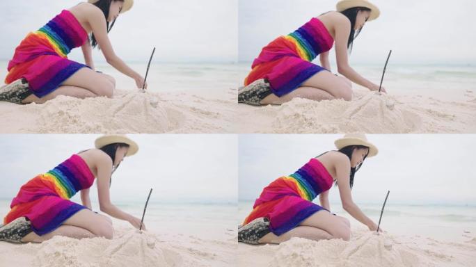 穿着太阳帽的亚洲俏皮女人夏季彩虹连衣裙坐下来玩沙子，人们在海滩上建造沙堡，假期独自玩耍，风险管理，想