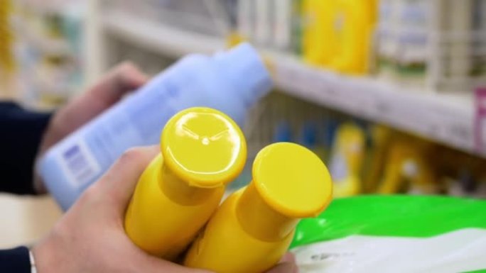 特写镜头在买家手中黄色的塑料瓶，配有儿童洗发水。在超市购买个人护理产品。商店里的肥皂和洗发水的选择