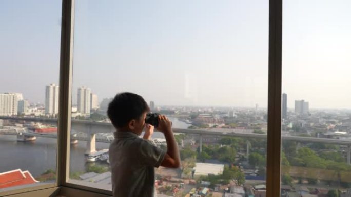 亚洲孩子在曼谷的天际线用双筒望远镜探索。探索和发现的概念