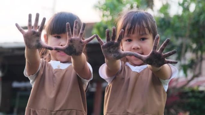 亚洲兄弟姐妹在花园里玩耍，炫耀他们肮脏的泥手。