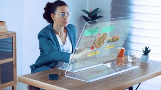 女人使用带有透明显示屏的计算机在网上商店订购食品。兴奋的女人在网上采摘快餐