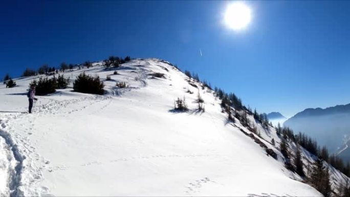 女人背着背包到达弗赖贝格的山顶十字路口，在奥地利卡林西亚的卡拉万克斯的白雪皑皑的山峰上享有风景。泽尔